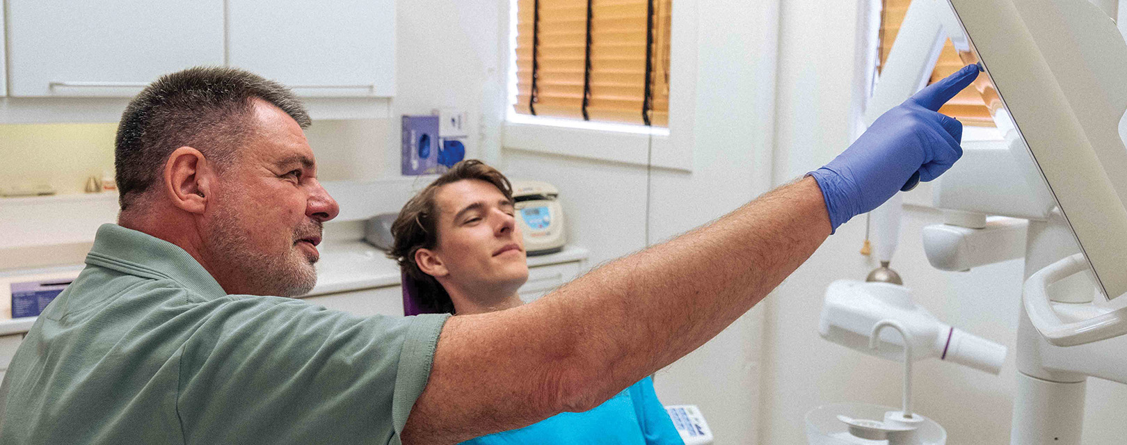 Tandlæge Per Hugo peger på skærm og patient kigger med fra stolen
